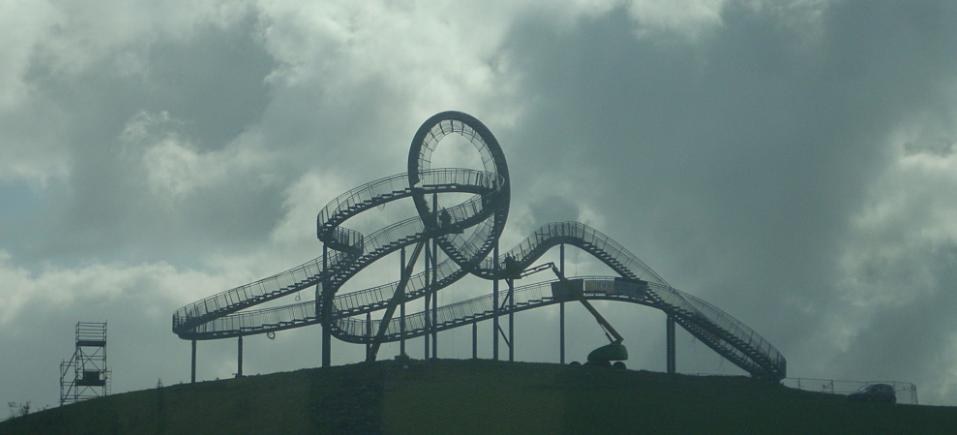 Eine Achterbahn auf dem Gipfel eines Hügels mit einem bewölkten Himmel, umgeben von Stützpfählen und -strukturen.