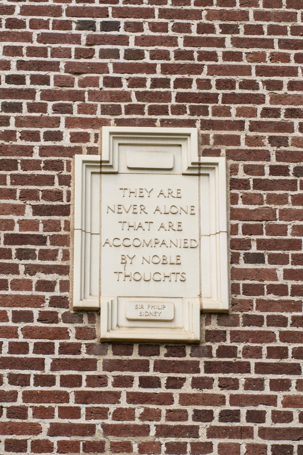 Steintafel auf einer Ziegelwand mit der eingravierten Inschrift "Sie sind nie allein, die von edlen Gedanken begleitet sind." in fetter Schrift.