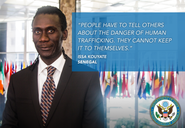 Mann im Anzug und Krawatte vor Flaggen, mit Text auf der rechten Seite: "Menschen müssen anderen von der Gefahr der Menschenhandel erzählen, sie können es nicht für sich behalten."