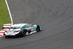 Ein silberner Mercedes-AMG GT3-Rennwagen auf einer Rennstrecke mit Text auf der Karosserie und Gras links daneben.