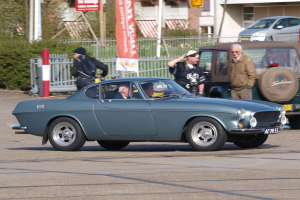 Eine Gruppe von Autos fährt auf einer Straße mit Passagieren, flankiert von Gebäuden, Bäumen und verschiedenen Straßenobjekten, über einer sichtbaren Straße.