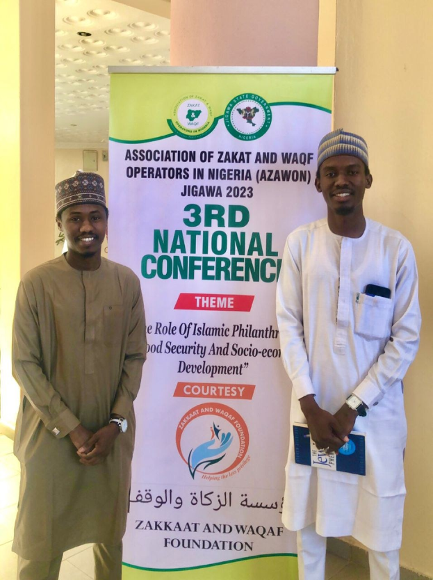 Zwei Männer stehen nebeneinander vor einem Banner mit der Aufschrift "3. Nationaler Kongress" mit einer Säule und Deckenleuchten im Hintergrund.