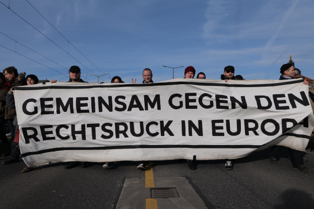 Gruppe von Menschen mit einem Banner "Gemeinsam gegen den Rechtsextremismus in Europa" während einer Protestaktion gegen die Europäische Union, mit Straßeninfrastruktur und Gebäuden im Hintergrund.