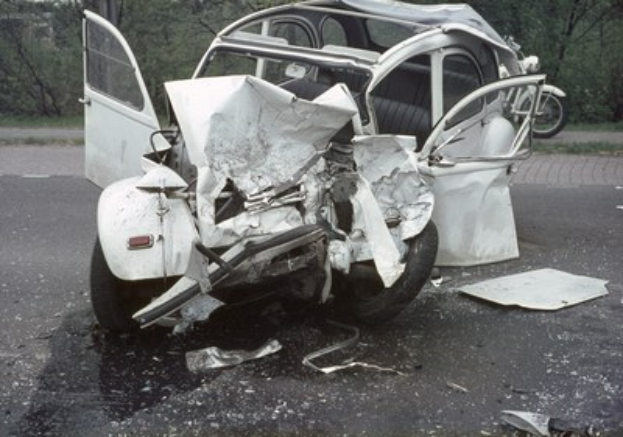 Schwerbeschädigte Frontpartie eines Wagens, der an der Stra√enseite mit Bäumen und einem Gebäude im Hintergrund steht.