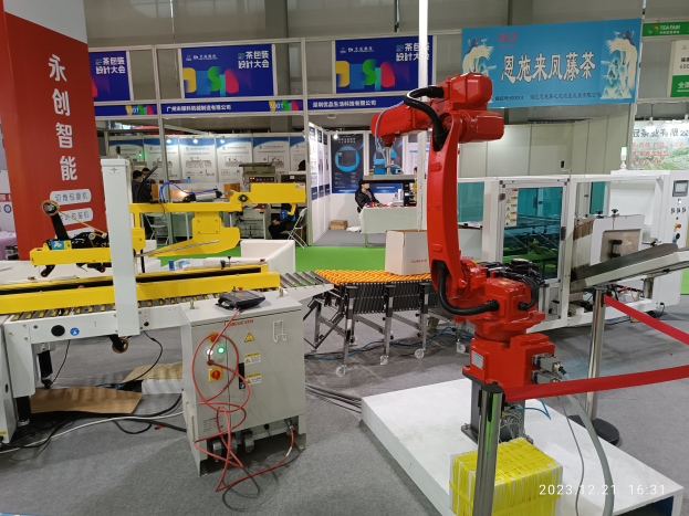 Gruppe von Robotern auf einem Tisch in einer Fabrikumgebung umgeben von Maschinen, Kabeln, Leiterplatten und Menschen im Hintergrund.