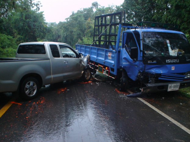 Ein schwer beschädigtes Lkw mit eingedrückter Front und verbeulter Karosserie liegt am Straßenrand, umgeben von Bäumen unter einem klaren blauen Himmel.