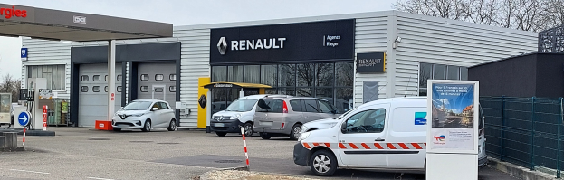 Renault-Vertretung mit parkenden Autos vorne, Metallzaun, Texttafel, Pfosten, Schild, Bäume und bewölkter Himmel.