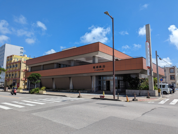 Großes Gebäude mit zahlreichen Fenstern, als Universität von Hong Kong Hauptsitz identifiziert, umgeben von Straßeninfrastruktur, Fahrzeugen und Grünflächen unter einem bewölkten Himmel.