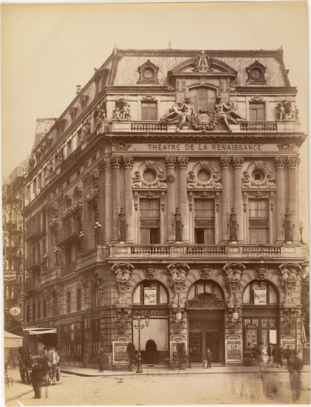 Schwarz-weiß-Foto des Théâtre de la Renaissance in Paris mit seiner prächtigen Fassade mit Fenstern, Säulen, Bögen und Skulpturen, mit ein paar Menschen und Fahrzeugen auf der Straße davor und dem Himmel im Hintergrund.
