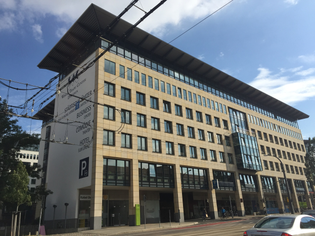 Großes modernes Gebäude mit zahlreichen Fenstern, beschriftet als 'Stadthalle Center for Business', umgeben von Bäumen und städtischer Infrastruktur in Köln, Deutschland.