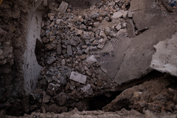 Einstürzendes Gebäude mit einem großen Loch im Boden, umgeben von Trümmern und einem sichtbaren Rohr, das Erdbebenschäden anzeigt.