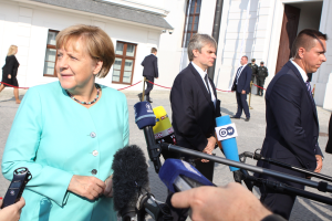 Bundeskanzlerin Angela Merkel spricht vor der Kanzleramt in Berlin mit Reportern, umgeben von einer Gruppe von Menschen, einige halten Mikrofone, mit Gebäuden im Hintergrund.
