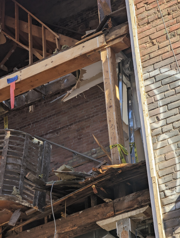 Ein teilweise abgerissenes Gebäude mit verstreuten Holzplanken und Trömmern sowie zerbrochene Fenster und Türen, was auf die Nachwirkungen des Abbruchs hindeutet.