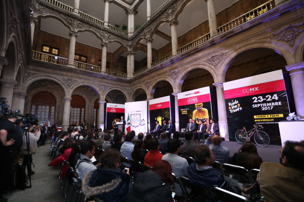 Eine Gruppe von Menschen, die an einem Tisch mit einem Podium und einem Mikrofon vor einer Menge, Kameras und Bannern sitzen, während einer Pressekonferenz für das CDMX 2017-Event.
