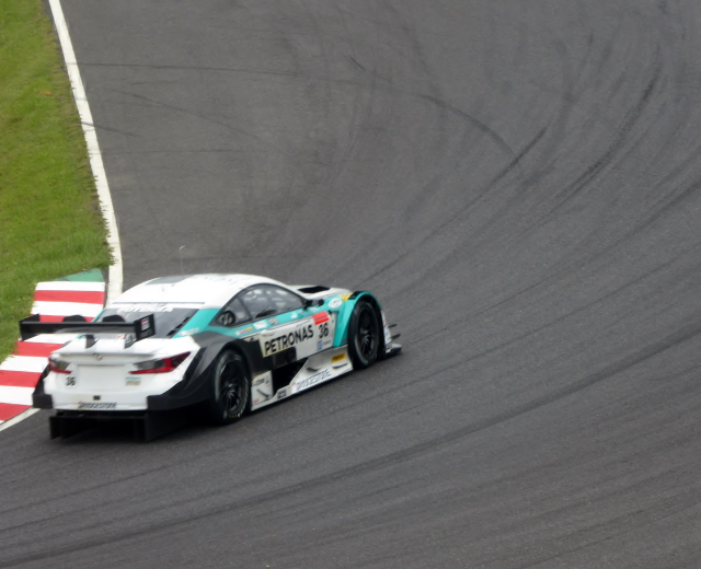 Ein silberner Mercedes-AMG GT3 Rennauto auf einer Rennstrecke mit Text auf seinem Körper und Gras links.