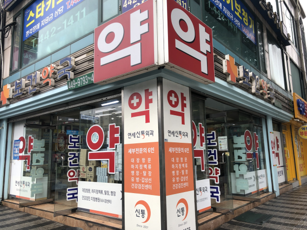 Außenansicht einer modernen Glaswand-Apotheke in Seoul, Südkorea, mit Text, der darauf hinweist, dass es sich um die erste Apotheke in der Stadt handelt.