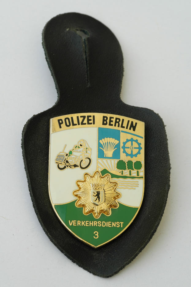 Ein schildförmiges Polizeibadges mit 'Polizei Berlin' in fetter schwarzer Schrift auf einem blauen Hintergrund, das ein weißes Stern in der Mitte und einen weißen Rand hat.