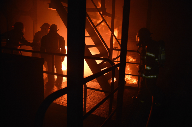 Feuerwehrleute in Schutzausrüstung vor einem brennenden Gebäude mit aufsteigendem Rauch in der Nacht
