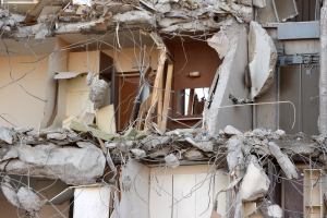 Ein teilweise abgerissener Bau mit zerbrochenen Wänden und verstreuten Trümmern, darunter Holzstücke, in einem Zustand des Verfalls.