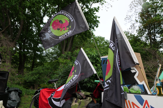 Ein Lastwagen beladen mit verschiedenen Gegenständen wie Fahnen, Taschen und Flaschen, mit einem Lautsprecher links daneben und Bäumen mit einem klaren blauen Himmel im Hintergrund.