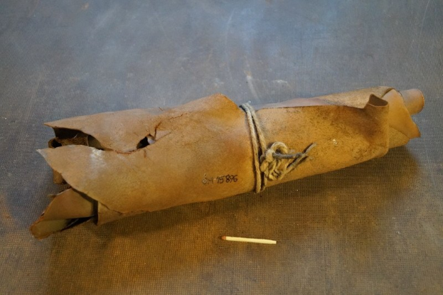 Ein brauner Papiertüte in Form einer Granate, mit einem Seil gebunden, liegt auf einem Tisch mit einer Zigarette daneben.