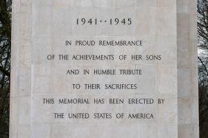Ein Denkmal mit einer Tafel, auf der "In stolzer Erinnerung an die Taten ihrer Söhne und in bescheidener Ehrung ihres Opfers" steht, vor einem Hintergrund aus Bäumen und einem klaren blauen Himmel.