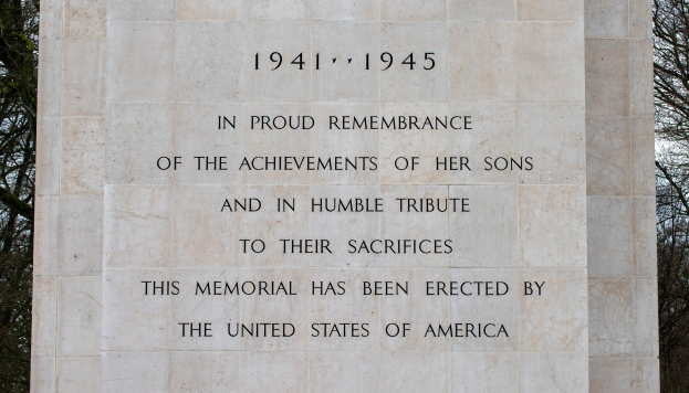 Ein Denkmal mit einer Tafel, auf der "In stolzer Erinnerung an die Taten ihrer Söhne und in bescheidener Ehrung ihres Opfers" steht, vor einem Hintergrund aus Bäumen und einem klaren blauen Himmel.