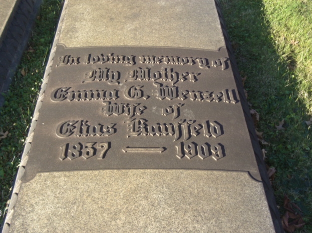 Grabstein auf einem Friedhof mit der Inschrift "In liebevoller Erinnerung an meine Mutter" umgeben von Gras und trockenen Blättern.