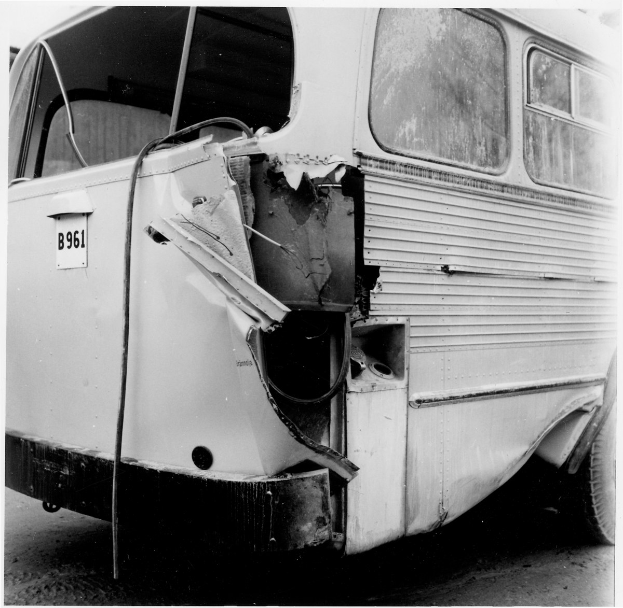 Schwarz-weiß-Foto eines Busses mit schwerer Frontschaden nach einer Autokollision, der auf der Straße geparkt ist.