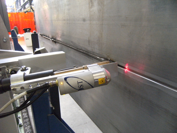 Hellstrahlendes Laserstrahlschneiden von Material auf einer Maschine in einer industriellen Fabrikumgebung, mit einer Wand auf der rechten Seite und Hintergrundobjekten.