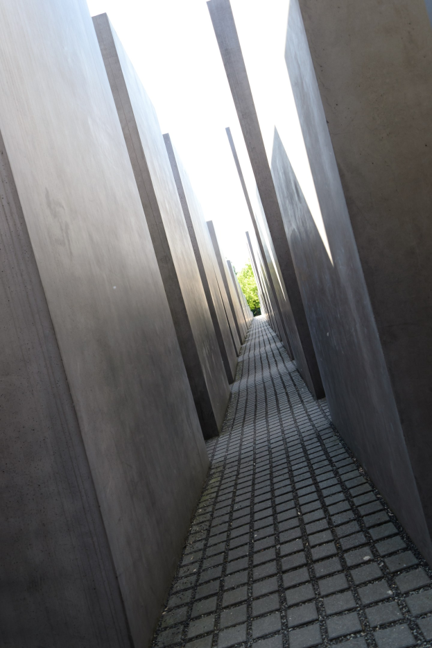 Betonplatten in einem Gittermuster bilden das Holocaust-Mahnmal für die ermordeten Juden Europas in Berlin mit Bäumen und einem klaren Himmel im Hintergrund.