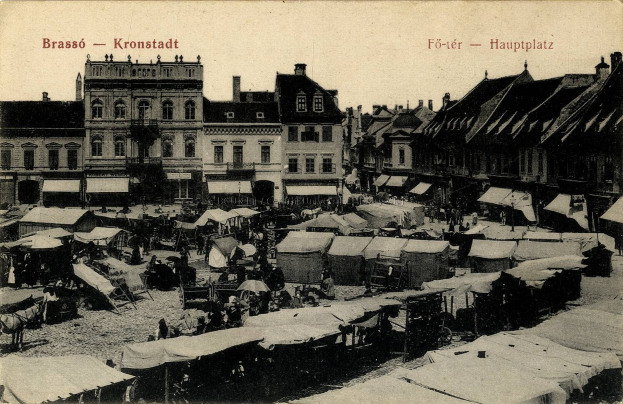 Schwarzes und weißes Foto eines belebten Marktes in Kronstadt, Deutschland, mit Menschen, Zelten und Gebäuden im Hintergrund.