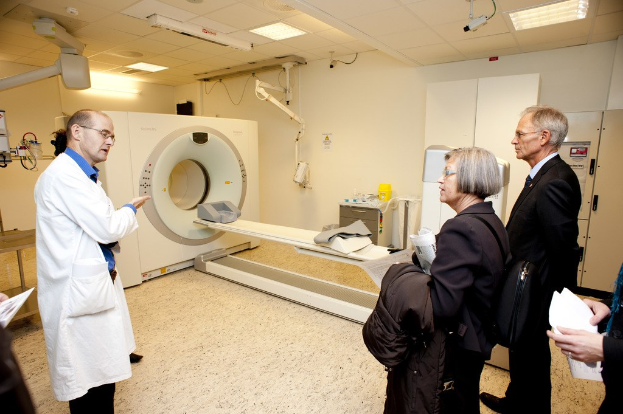 Arzt in weißer Uniform erklärt CT-Scan-Maschine zwei Personen in schwarzen Mänteln.