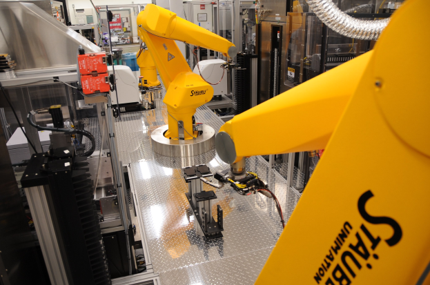 Ein gelber Roboter, der in einer industriellen Fabrikumgebung Maschinen bedient, mit sichtbaren Rohren und Beleuchtung.