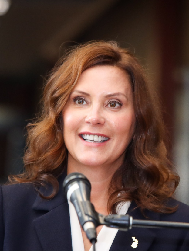 Eine Frau in Anzug und Krawatte, die in ein Mikrofon spricht, identifiziert als Michele Bachmann, mit einem unscharfen Hintergrund.