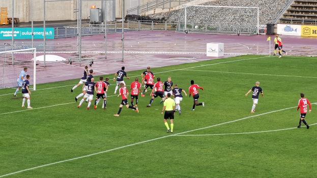 Eine Gruppe von Menschen spielt Fußball auf einem Feld mit Zuschauern in einem Stadion.