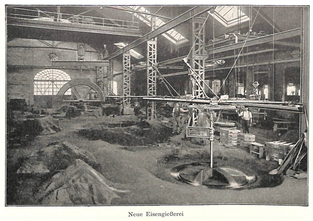 Schwarzes und weißes Foto einer historischen deutschen Fabrik mit Arbeitern, die Maschinen bedienen, umgeben von Metallstangen und -pfählen, beschriftet mit 'Neue Eisenglebeerei, die erste Fabrik in Deutschland' unten.