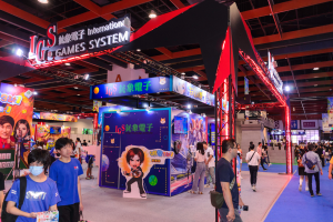 Eine Gruppe von Menschen geht durch einen Convention Hall mit Ständen, trägt Taschen und hält Gegenstände, mit vielen anderen im Hintergrund auf einer Gaming-Messe in China.