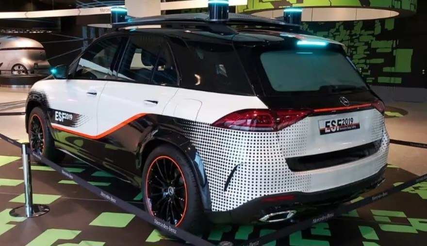 Mercedes-Benz E-Klasse Electric SUV auf der IAA in Frankfurt, umgeben von Absperrpollern mit Seilen und Lichtern, mit einem weiteren Fahrzeug und einer textbedruckten Wand im Hintergrund.