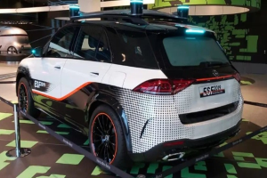 Mercedes-Benz E-Klasse Electric SUV auf der IAA in Frankfurt, umgeben von Absperrpollern mit Seilen und Lichtern, mit einem weiteren Fahrzeug und einer textbedruckten Wand im Hintergrund.