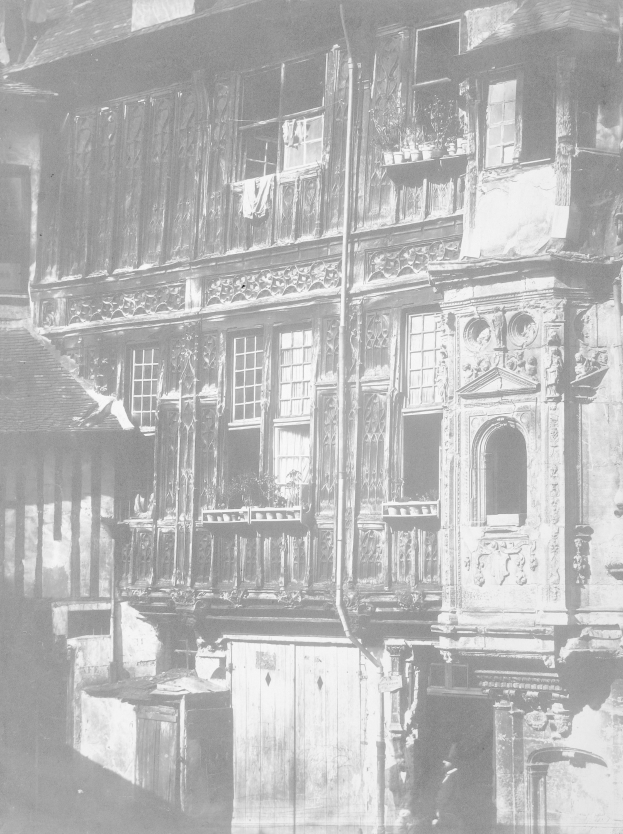 Altes Schwarz-Weiß-Foto eines mehrstöckigen Gebäudes mit zahlreichen Fenstern und Balkonen, das detaillierte Wand- und Türschnitzereien zeigt.