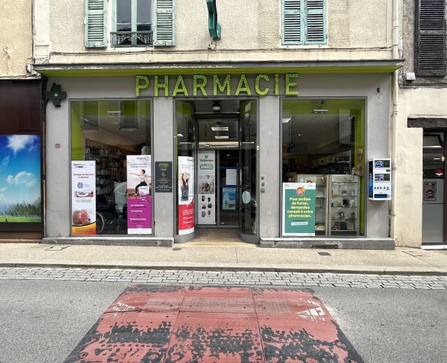 Apothekenfront mit Glaswänden und -türen, Plakate an den Innenwänden und eine Straße unten.
