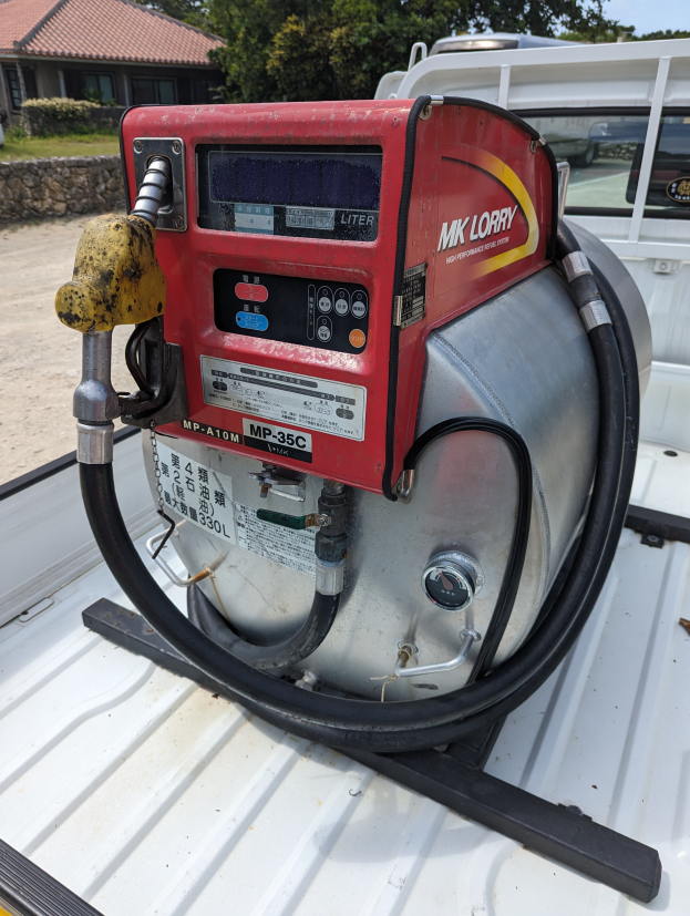 Ein Lastwagen mit einer Tankstelle auf der Ladefläche, umgeben von Bäumen, einem Haus und einem klaren blauen Himmel, ausgestattet mit einem Motor und einer Kraftstoffabgabe.