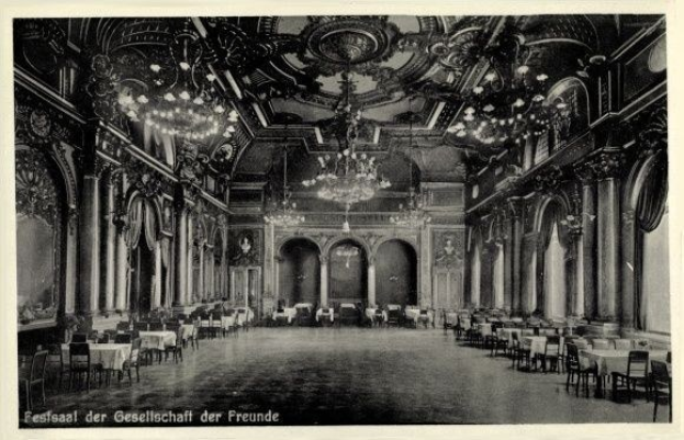 Schwarzes und weißes Foto eines großen Raums mit Tischen, Stühlen, Säulen, Bögen und Kronleuchtern, beschriftet mit "Festival der Gesellschaft der Freunde, Berlin" unten.