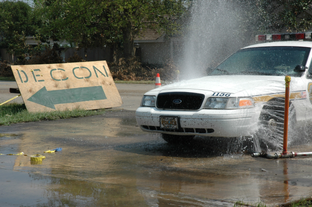 Ein Polizeiwagen f\ufffhrt durch eine Pf�tze, mit einem Schild, einer Verkehrsinsel und anderen Gegenst\ufffnden auf dem Boden, vor einem Hintergrund aus B\ufffumen, Geb\ufffuden und einem klaren blauen Himmel.