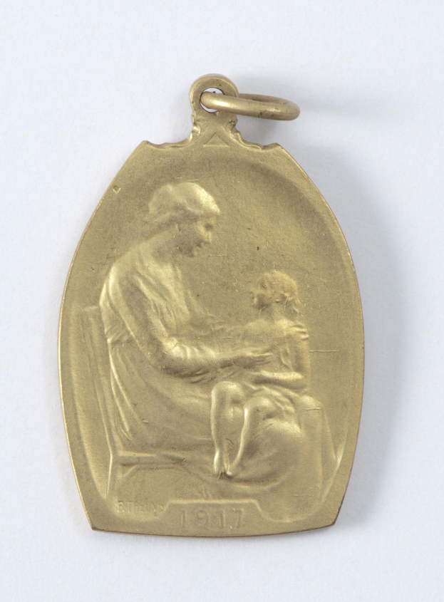 Goldmedaille mit einer Reliefdarstellung einer Frau in einem weißen Kleid mit einem Knoten im Haar, die ein Kind hält, beide schauen einander an, mit der Inschrift "Mutter und Kind" in Kursivschrift.