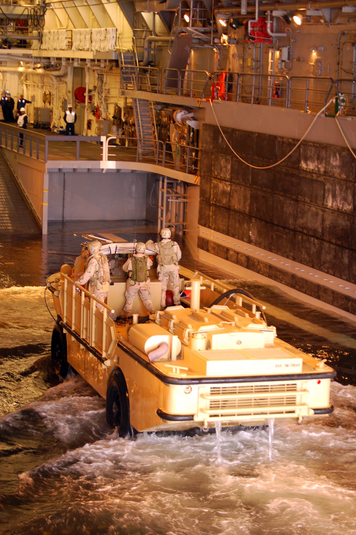 Amphibisches Fahrzeug fährt durch Wasser mit Helmträgern, nahe einer Wand und Hintergrundstrukturen einschließlich Geländern, Lampen und Rohren.