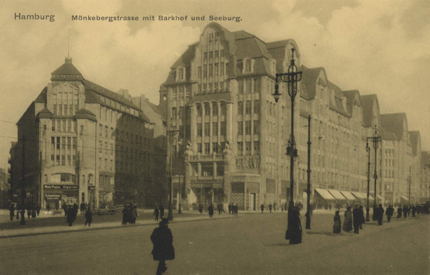 Schwarzes und weißes Foto von Menschen, die eine Straße in Hamburg, Deutschland, entlanggehen, mit Gebäuden, Straßenlaternen, Lichtern und Kraftfahrzeugen, die entlang der Straße aufgereiht sind, unter einem bewölkten Himmel.