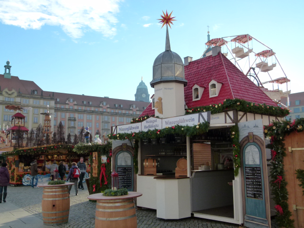 Ein geschäftiger Weihnachtsmarkt in Nürnberg, Deutschland mit Menschen um geschmückte Stände, festliche Lichter, ein Riesenrad im Hintergrund und ein Schild auf der rechten Seite.