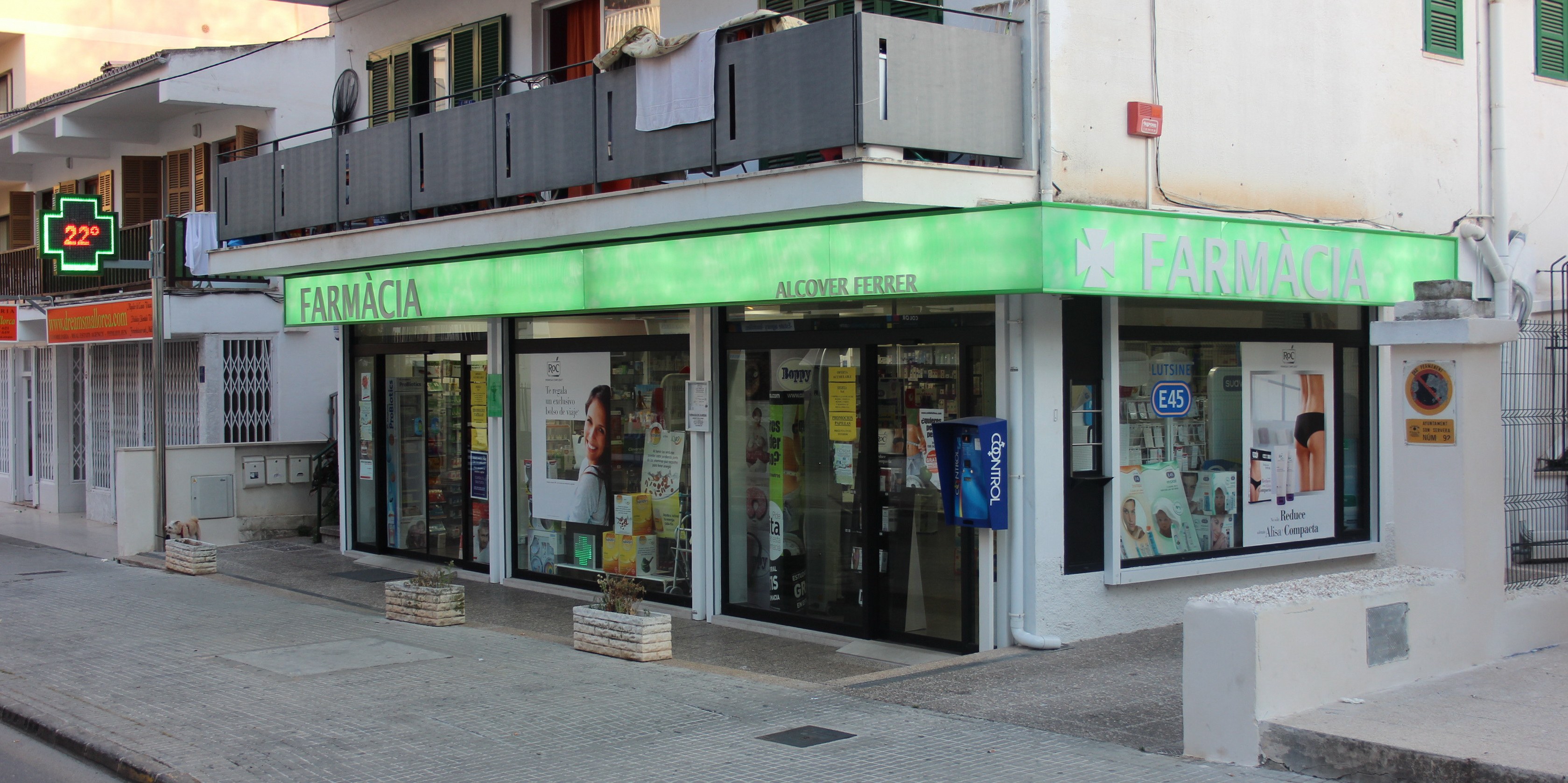 Eine Straßenansicht einer Apotheke mit umliegenden Gebäuden, Fahrzeugen und einem klaren Himmel.